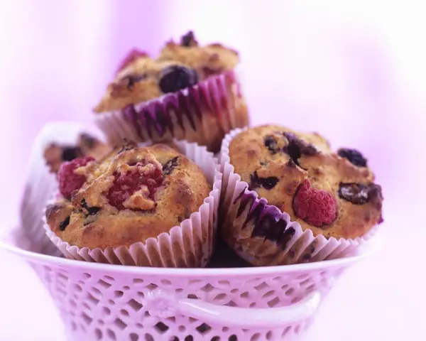 Saftige Muffins mit Obst und Joghurt, garniert mit frischen Himbeeren und Blaubeeren, in einem rosa Körbchen.