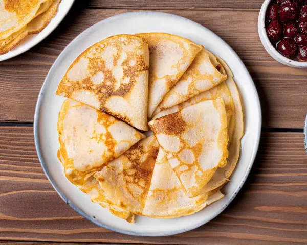 Omas Pfannkuchen-Rezept: goldbraune, gefaltete Pfannkuchen auf einem Teller, daneben eine Schüssel mit Kirschen.
