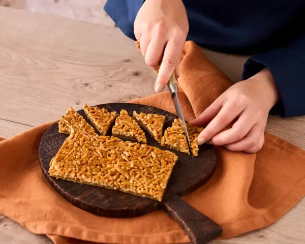 Ein Nussecken Rezept wird hier gezeigt. Eine Person schneidet die süßen Nussecken auf einem Holzbrett.