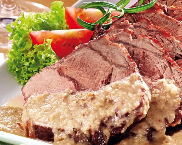 Saftiger Sauerbraten, perfekt für Ihr nächstes Sauerbraten Rezept, serviert mit frischem Salat und Tomaten.