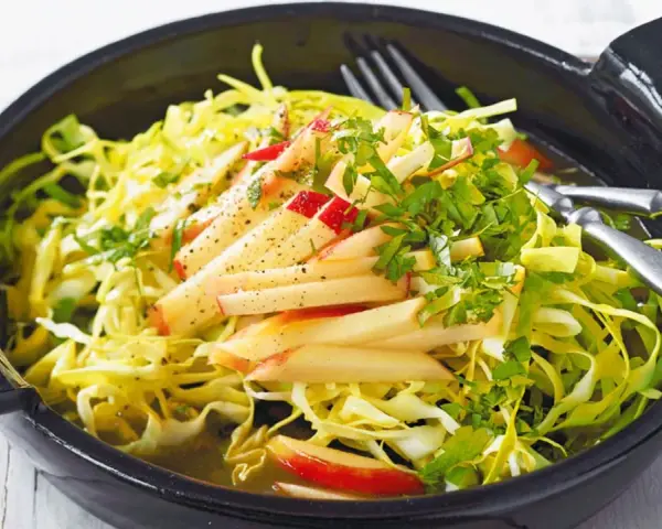 Frischer Spitzkohl Salat mit Apfelspalten und Kräutern, appetitlich in einer schwarzen Schüssel serviert.