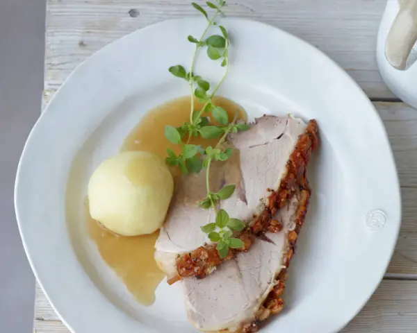 Ein knuspriger Schweinebraten mit Soße und Klößen, perfekt für ein deftiges Schweinebraten Rezept. Frisch garniert mit Kräutern.