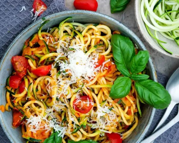 Herzhafte Zucchini-Nudeln mit Tomaten und Basilikum, bestreut mit Parmesan. Ein leichter Genuss!