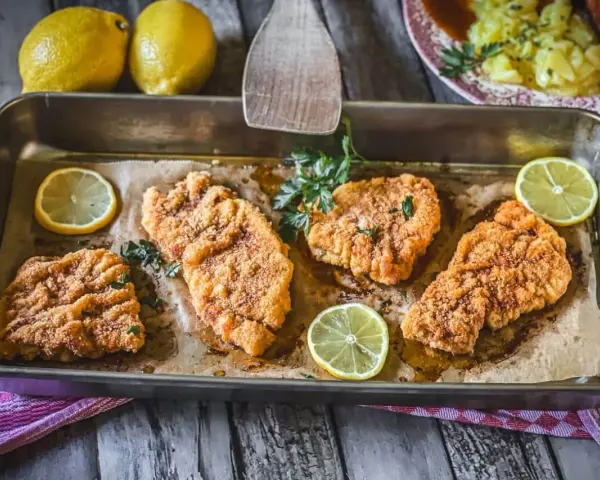 Saftiges Schnitzel im Backofen, goldbraun paniert, mit frischer Petersilie und Zitronenspalten garniert. Ein Genuss!