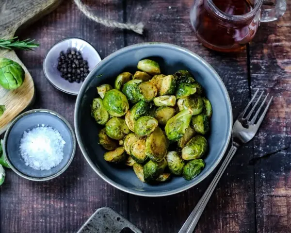 Gerösteter Rosenkohl in einer Schüssel, bereit für leckere Rezepte mit Rosenkohl. Daneben Salz, Pfeffer und ein Glas Sirup.