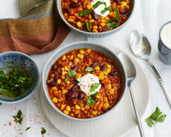 Herzhaftes Chili sin Carne mit Mais, Bohnen und Linsen, garniert mit einem Klecks Sauerrahm und frischer Petersilie.
