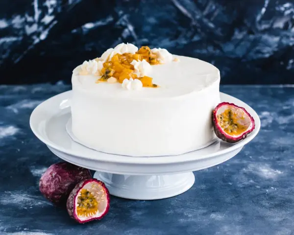 Eine weiße Maracuja Torte mit frischer Maracuja-Frucht und Sahnetupfern, umgeben von ganzen und halbierten Maracujas.