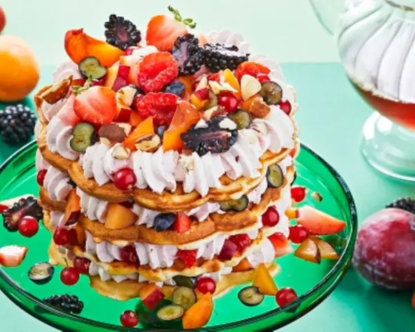 Eine mehrstöckige Waffeltorte mit Mascarpone-Creme, Beeren, Pfirsichen und Nüssen, garniert mit frischen Früchten.