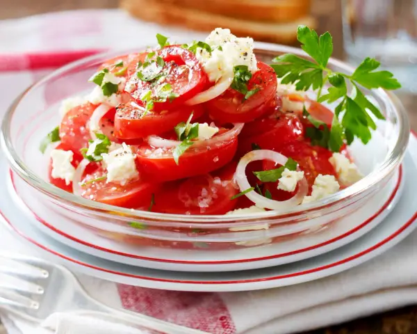 Frischer Tomaten Feta Salat mit Zwiebelringen und Petersilie, garniert mit schwarzem Pfeffer und Meersalz.
