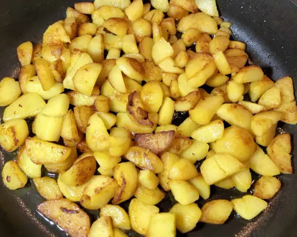 Goldbraune bratkartoffeln aus gekochten kartoffeln brutzeln in der Pfanne. Sie sind knusprig und duften herrlich.