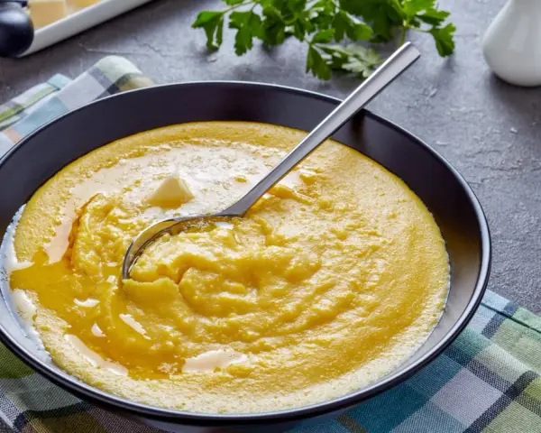 Cremige Polenta mit Butter, ein einfaches und köstliches polenta rezept, serviert in einer schwarzen Schüssel auf kariertem Tuch.