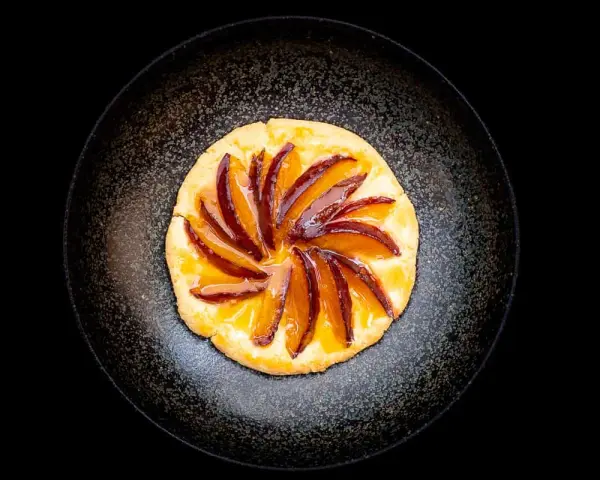 Eine köstliche Zwetschgen Tarte, mit saftigen Zwetschgenspalten, kunstvoll auf einem knusprigen Teig arrangiert und mit glänzendem Sirup überzogen.