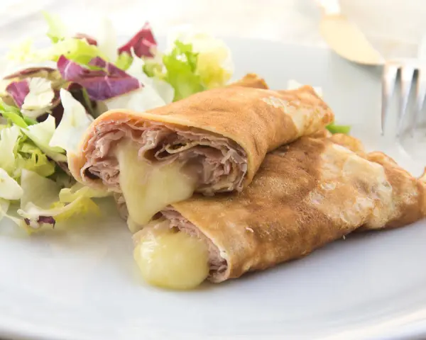 Zwei herzhafte Pfannkuchen mit Schinken und geschmolzenem Käse, serviert mit einem frischen Salat.