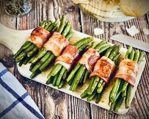 Grüne Bohnen, umwickelt mit knusprigem Speck, ein köstliches Speckbohnen Rezept, serviert auf einem Holzbrett.