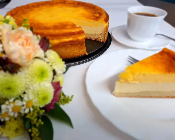 Ein köstliches Eierschecke-Rezept: Ein goldbrauner Kuchen mit cremiger Füllung, daneben eine Tasse Kaffee und ein Blumenstrauß.