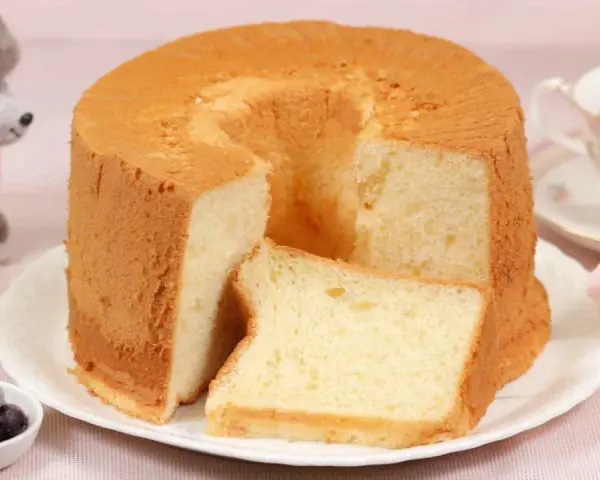 Ein luftiger Chiffon-Kuchen mit einer Scheibe daneben, serviert mit Beeren und Tee.