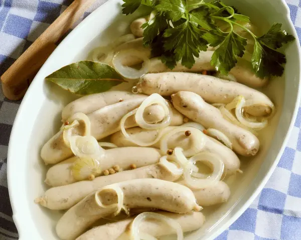 Saure Zipfel in einer Schüssel mit Zwiebelringen, Lorbeerblatt und Petersilie.