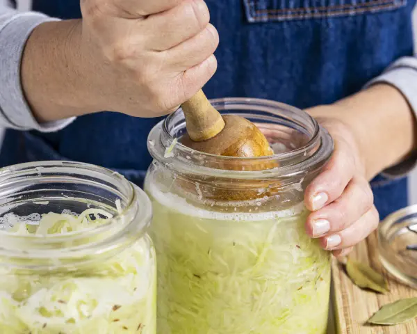 Hände pressen Kohl für ein einfaches Sauerkraut Rezept in ein Glas.