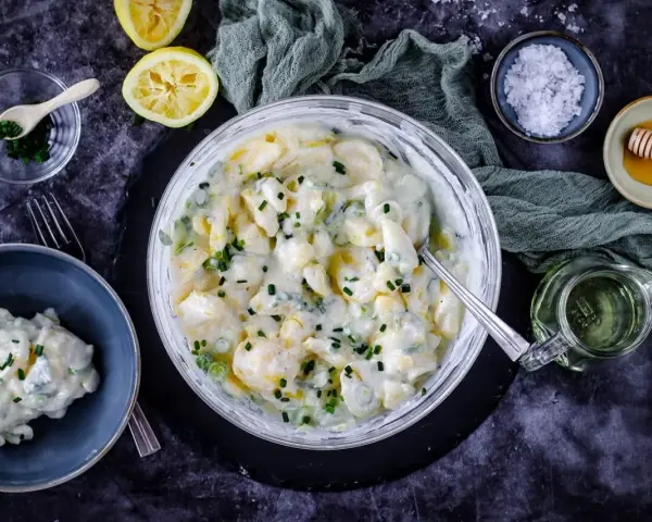 Cremiger Kartoffelsalat mit Joghurt, garniert mit Schnittlauch. Dazu Zitrone, Honig und grobes Salz.