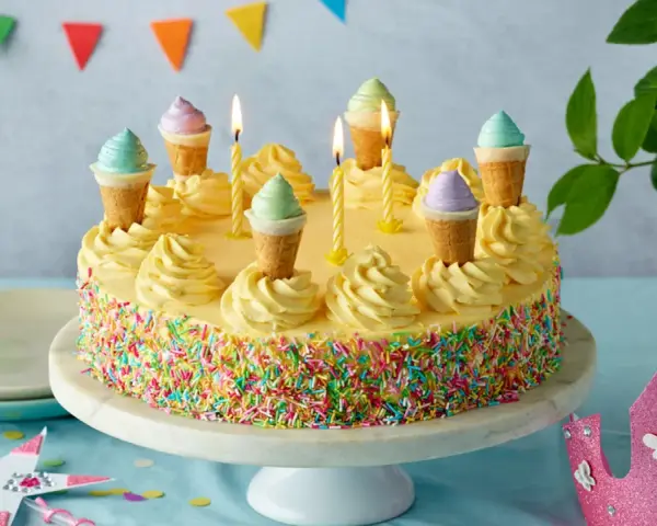 Bunte Torte mit Streuseln und Eiswaffel-Deko, perfekt für kinder torten rezepte einfach. Kerzen brennen, eine märchenhafte Feier beginnt.