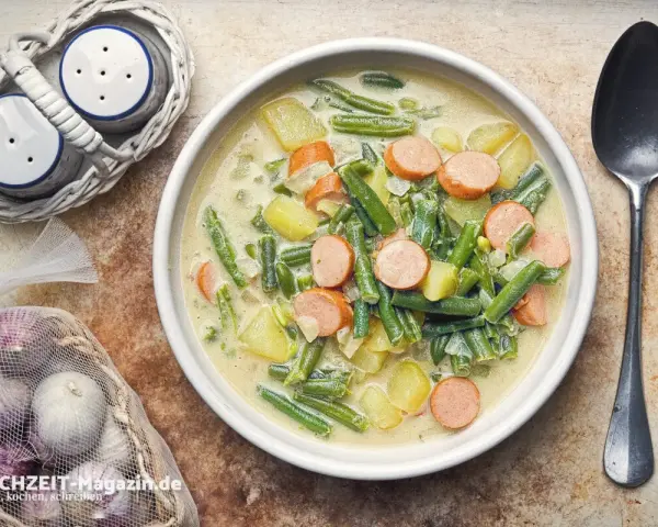 Herzhafte Bohnen-Kartoffel-Suppe mit Würstchen, ein Klassiker unter den Bohnen Rezepten. Dazu Salz- und Pfefferstreuer und frischer Knoblauch.