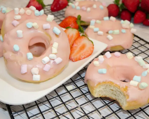 Leckere Donuts mit rosa Glasur und Marshmallows, perfekt für ein schnelles Donuts Rezept aus dem Backofen. Frische Erdbeeren garnieren das süße Gebäck.