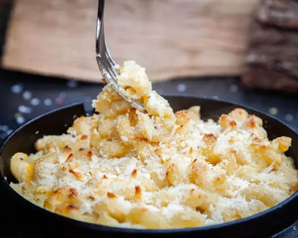 Ein Gabel hebt cremiges, überbackenes Mac n Cheese aus einer Pfanne. Dieses amerikanische Original-Rezept ist ein Genuss!