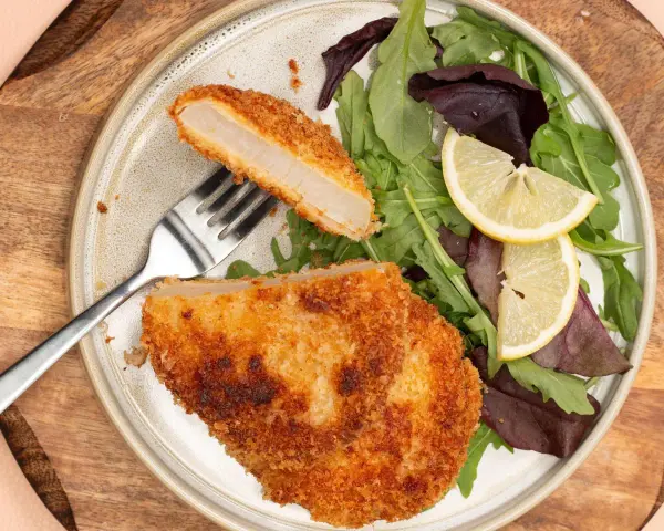 Knuspriges Kohlrabi-Schnitzel mit Salat und Zitrone auf einem Teller.