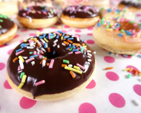 Bunte Streusel auf Schokoladen- und Zuckerguss-Donuts, die an ein leckeres Donut Teig Rezept erinnern.