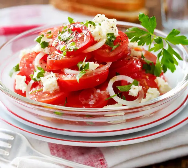 Frischer Tomaten Feta Salat mit Zwiebelringen und Petersilie, garniert mit schwarzem Pfeffer und Meersalz.