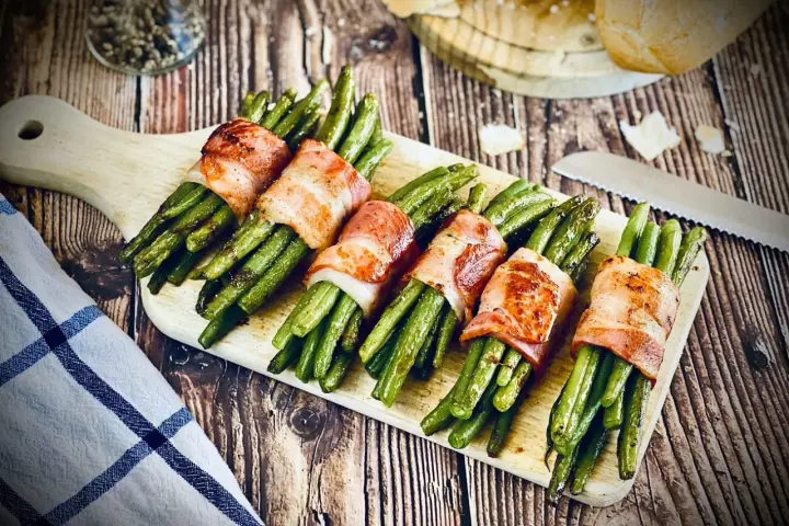 Grüne Bohnen, umwickelt mit knusprigem Speck, ein köstliches Speckbohnen Rezept, serviert auf einem Holzbrett.
