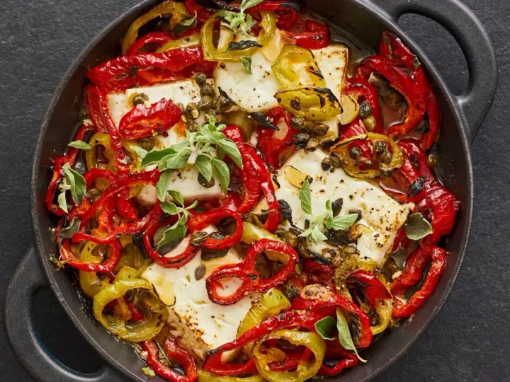 Gebackener Feta mit bunten Paprikastreifen, Kapern und frischen Kräutern in einer gusseisernen Pfanne.