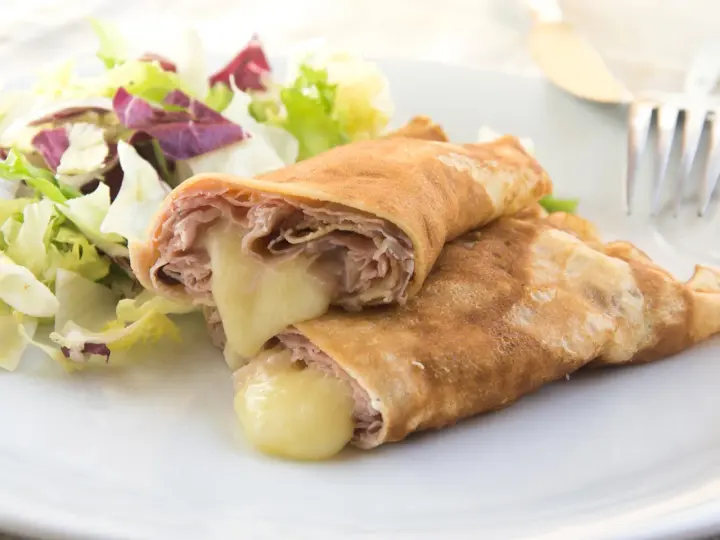 Zwei herzhafte Pfannkuchen mit Schinken und geschmolzenem Käse, serviert mit einem frischen Salat.