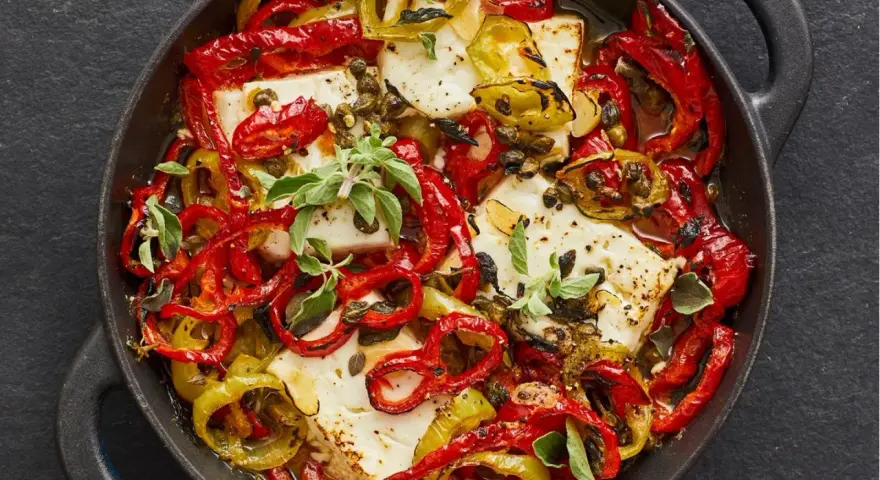 Gebackener Feta mit bunten Paprikastreifen, Kapern und frischen Kräutern in einer gusseisernen Pfanne.