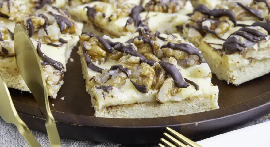 Ein "friss dich dumm kuchen" mit cremiger Füllung, Walnüssen und Schokoladendrizzle auf einem Holztablett. Goldene Gabel und Messer liegen daneben.