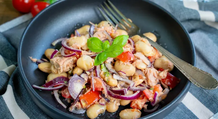 Herzhafter Thunfischsalat mit weißen Bohnen, Tomaten und roten Zwiebeln, garniert mit Basilikum. Ein köstlicher und einfacher Salat.
