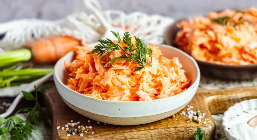 Karottensalat mit cremigem Dressing, wie im Restaurant. Frisch geriebene Karotten, garniert mit Dill, auf einem Holzbrett.
