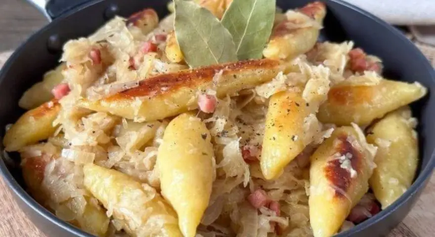 Schupfnudeln mit Sauerkraut, Speck und Lorbeerblättern in einer Pfanne. Ein herzhaftes Gericht, das zum Genießen einlädt.