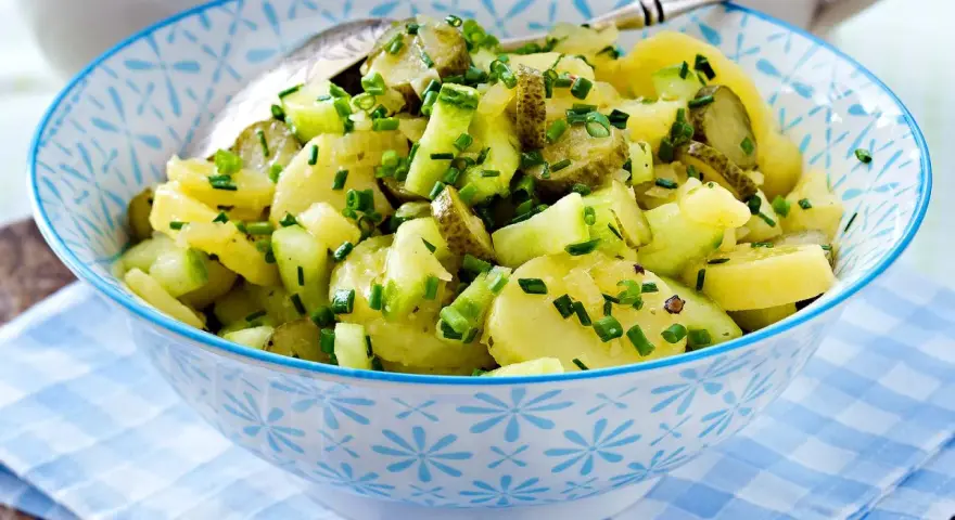 Schüssel mit Kartoffelsalat mit Gurken und Schnittlauch, garniert mit frischen Kräutern.