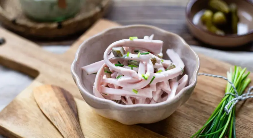 Schmackhaftes Fleischsalat-Rezept mit Gurkenstückchen und Schnittlauch garniert, serviert in einer Schale auf einem Holzbrett.
