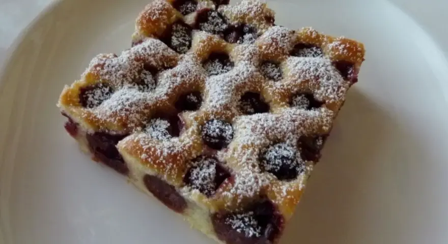 Zwei Stücke Kirschstreuselkuchen vom Blech, mit Puderzucker bestäubt, auf einem weißen Teller.