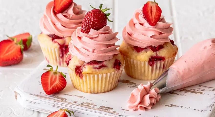 Erdbeer Cupcakes mit rosa Frosting und frischen Erdbeeren. Ein Spritzbeutel zeigt, wie die leckeren Erdbeer Cupcakes entstehen.
