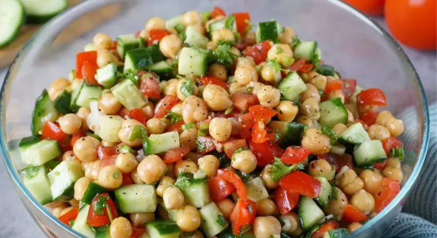 Frischer Kichererbsen Salat mit Gurken, Tomaten und Kräutern in einer Glasschüssel. Ein leichter und gesunder Genuss.