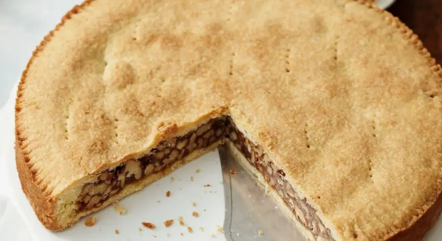 Eine köstliche Engadiner Nusstorte mit goldbraunem Teig und einer reichhaltigen Nussfüllung, gerade angeschnitten.
