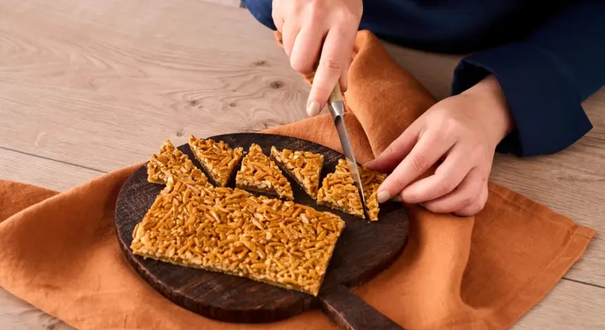 Ein Nussecken Rezept wird hier gezeigt. Eine Person schneidet die süßen Nussecken auf einem Holzbrett.