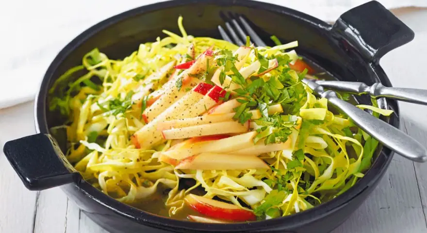Frischer Spitzkohl Salat mit Apfelspalten und Kräutern, appetitlich in einer schwarzen Schüssel serviert.