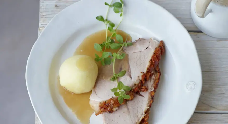 Ein knuspriger Schweinebraten mit Soße und Klößen, perfekt für ein deftiges Schweinebraten Rezept. Frisch garniert mit Kräutern.