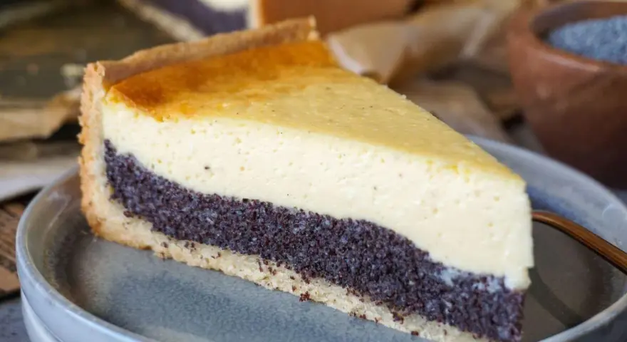 Ein Stück Mohnkuchen mit cremigem Käse-Topping und Mohnback-Schicht auf einem grauen Teller.