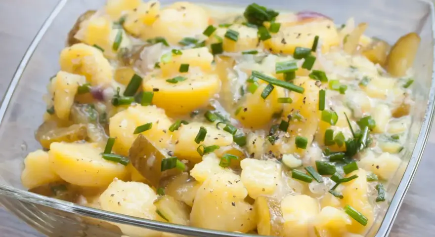 Ein köstlicher Kartoffelsalat ohne Mayo, mit Gurkenstücken und frischem Schnittlauch garniert, in einer Glasschüssel.