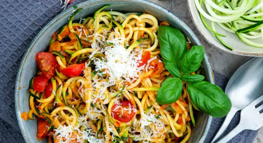 Herzhafte Zucchini-Nudeln mit Tomaten und Basilikum, bestreut mit Parmesan. Ein leichter Genuss!